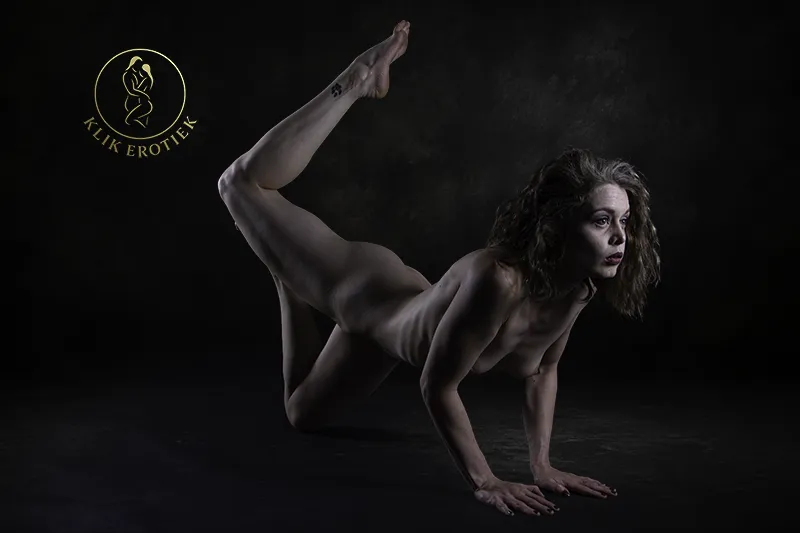 Artistieke naaktfotografie van een vrouw in sfeervolle studiobelichting.
